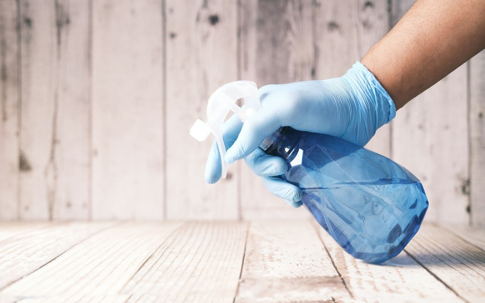 Deep cleaning a wooden floor with spray and gloves